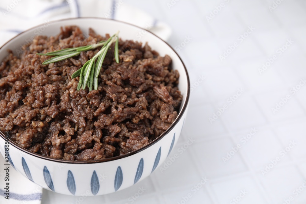 Fried ground meat in bowl and rosemary on white tiled table, closeup. Space for text Fried ground meat in bowl and rosemary on white tiled table, closeup. Space for text