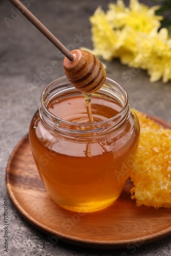 Pouring sweet golden honey from dipper into jar at grey table