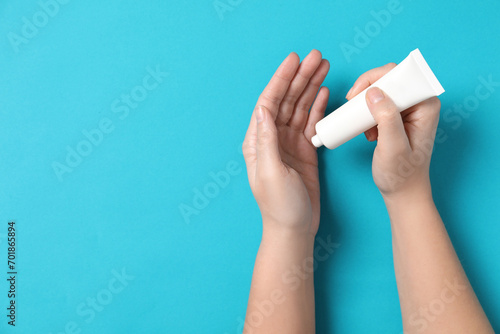 Woman applying cosmetic cream from tube onto her hand on light blue background, top view. Space for text
