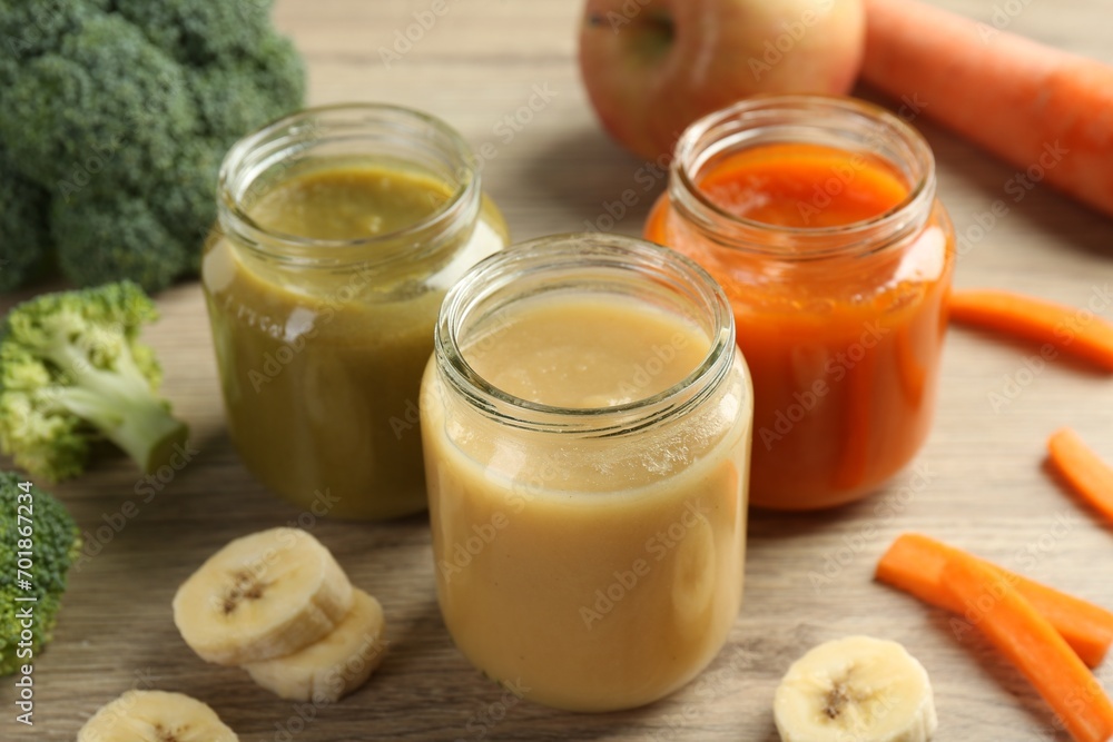 Tasty baby food in jars and ingredients on light wooden table, closeup Tasty baby food in jars and ingredients on light wooden table, closeup