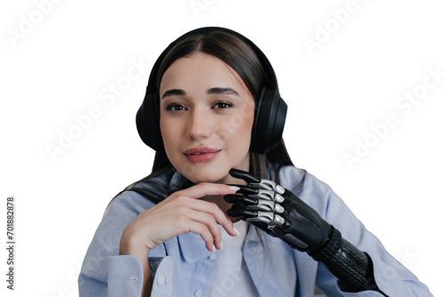 Cyte brunette girl with biomechanics hand in headphones listening music looking at camera in light blue shirt. Calm girl with disability touching her hand prosthesis by another hand. Limb prosthesis. photo