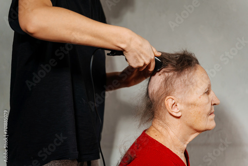 shaving woman because of a cancerous tumor. removal of hair on the head with an electric razor before surgery. hair loss due to cancer. shaving the grandmother's head before a course of chemo therapy