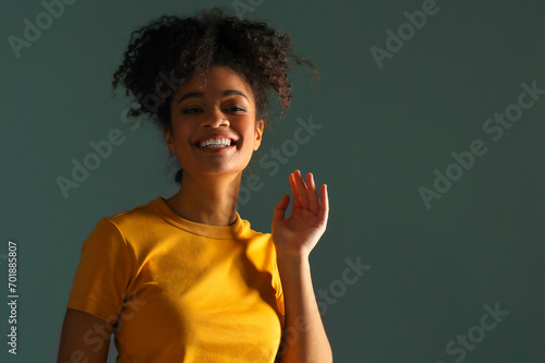 Beautiful happy African American ethnicity woman in yellow tshirt raising hand in greeting