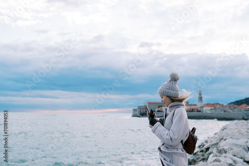 Girl is standing on the beach and looking at her smartphone. Side view