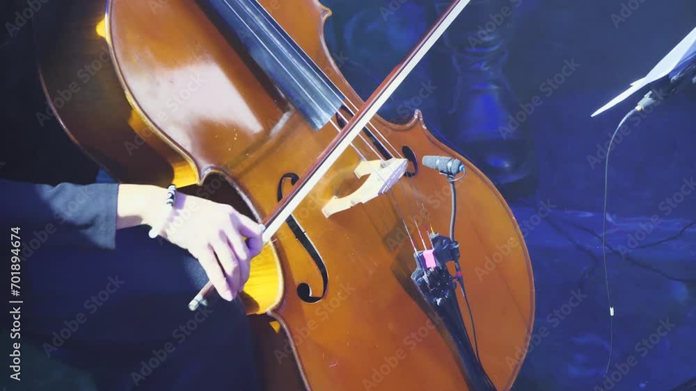 Close-up of cello playing. A woman's hand with a bow playing classical music on a cello. Bright light show. Slow motion