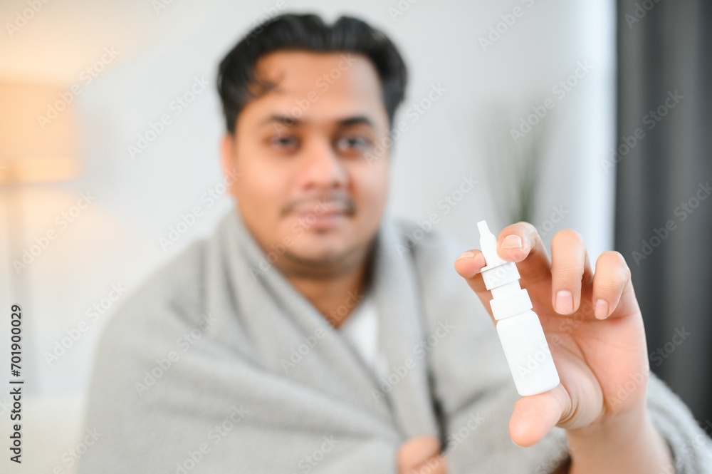 rhinitis, medicine and healthcare concept - sick indian man in blanket using nasal spray at home rhinitis, medicine and healthcare concept - sick indian man in blanket using nasal spray at home