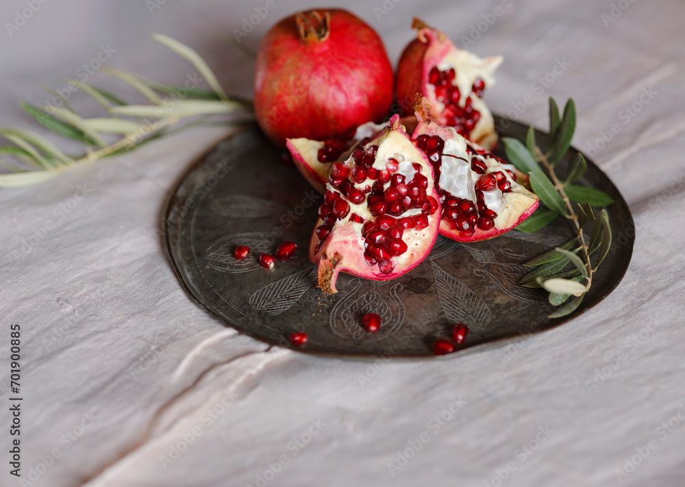 Image of Still Life with Turkish Pomegranate and olive branch on old retro plate. Dark wood background, antique copper plate. Fresh ripe whole pomegranates, opened pomegranate and seeds Image of Still Life with Turkish Pomegranate and olive branch on old retro plate. Dark wood background, antique copper plate. Fresh ripe whole pomegranates, opened pomegranate and seeds