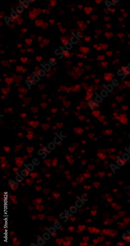 Red hearts slow falling down on black vertical background.