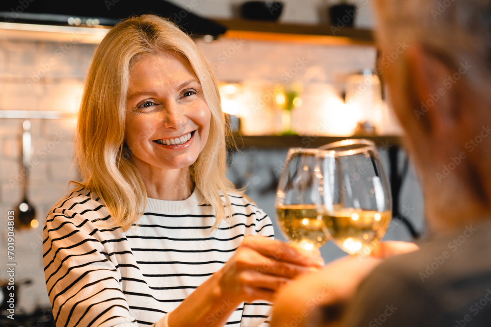 Cheerful happy mature couple having romantic dinner in the kitchen with glasses of wine, focused on the woman