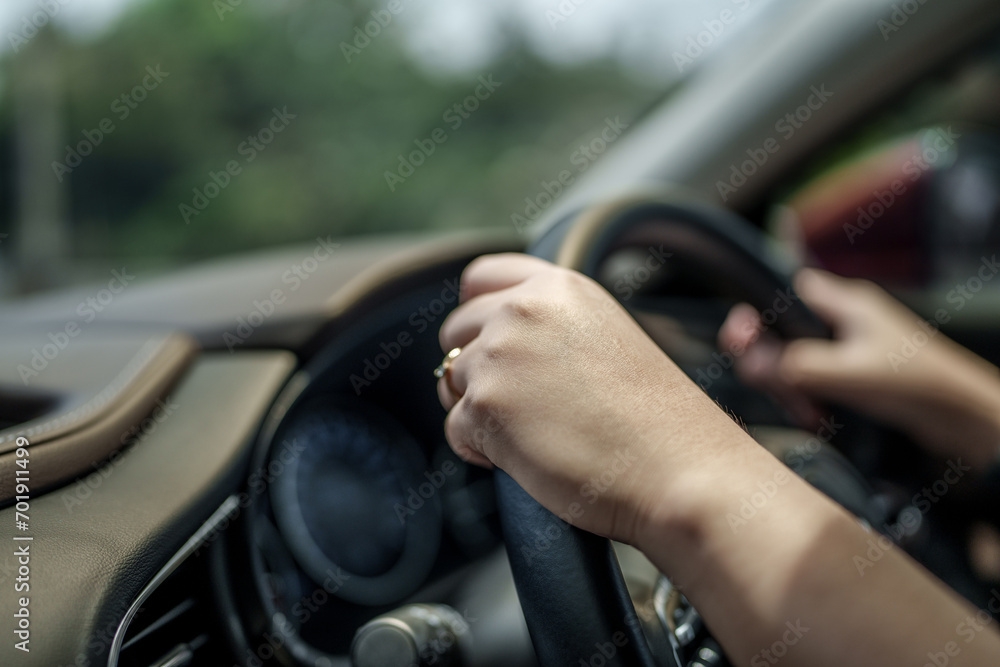 Close up hands of driver holding steering wheel in car, road trip, driving on local road.