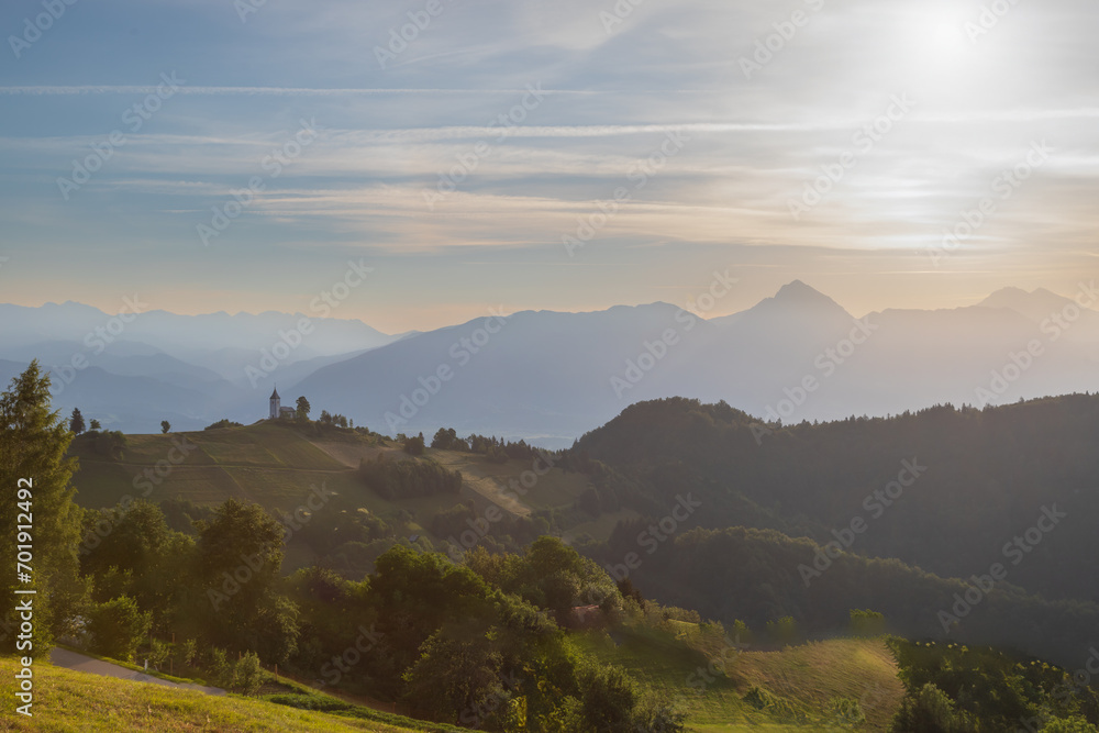 Church of Saint Primoz in Jamnik village, Slovenia, Europe. The church is on the ridge of the mountains. Sunrise, mountain peaks in the background. Church of Saint Primoz in Jamnik village, Slovenia, Europe. The church is on the ridge of the mountains. Sunrise, mountain peaks in the background.