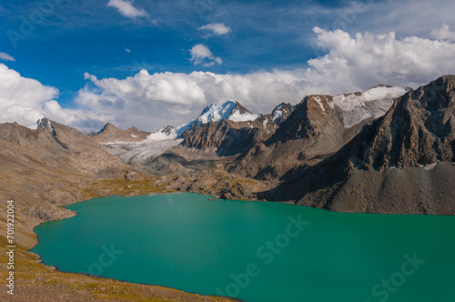 Alakel, a turquoise lake visited by tourists, lies cradled by rugged mountains under a clear blue sky, dotted with snow