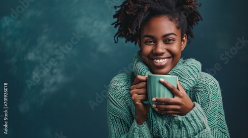 portrait of happy young woman with cup of coffee isolated on navy background with copy space, smiling African American woman in mint green sweater holding coffee mug and enjoy herself. photo