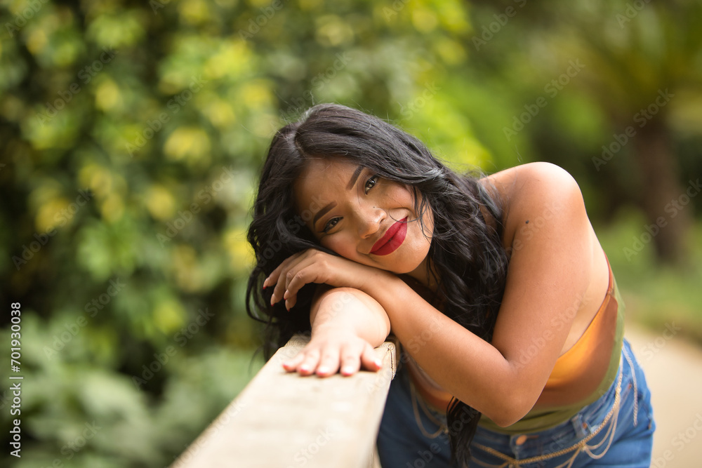 Portrait of South American woman, young, beautiful, brunette, with colorful top and jeans leaning on a wooden railing with tender, pure, dreamy look. Concept of beauty, trend, ethnicity, diversity. Portrait of South American woman, young, beautiful, brunette, with colorful top and jeans leaning on a wooden railing with tender, pure, dreamy look. Concept of beauty, trend, ethnicity, diversity.