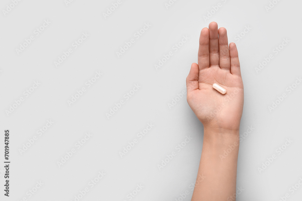 Naklejka premium Female hand with white capsule on light background
