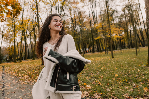 Attractive pretty woman walking outdoor, portrait of young lady in warm sunny autumn park season, fall, yellow orange red leaves, dressed leather wool fur jacket smiling having fun 