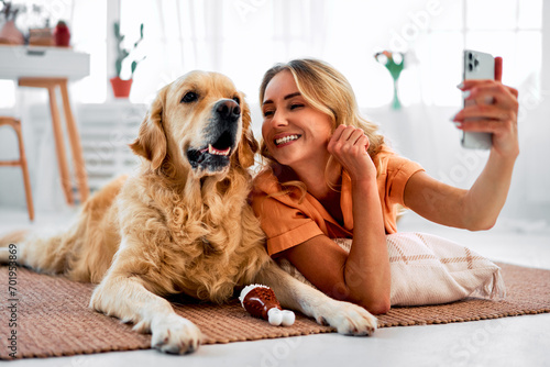 Fun with domestic animal. Loving pet owner taking selfie on smartphone while lying on floor near golden retriever. Cheerful female cuddling on best dog companion and enjoying daily interaction.