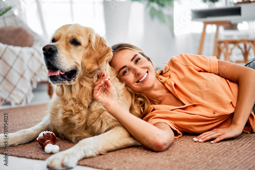 Love and affection. Beautiful young lady with blond hair resting on floor with lovely dog companion. Smiling caucasian woman enjoying home comfort while leaning back on fluffy golden retriever.