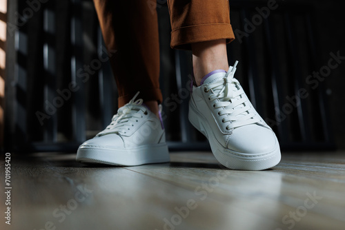 Comfortable women's sneakers on a flat sole with laces. Close-up of female legs in white perforated leather sneakers. Women's summer sneakers. Collection of women's leather shoes