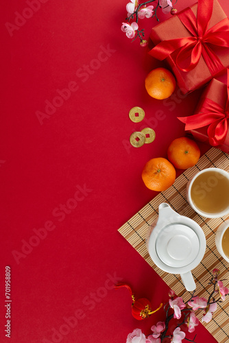 Enriching celebrations with the chinese New Year tea ceremony. Top view vertical shot of teapot, cups of tea, tangerines, red gift boxes, traditional chinese elements on red background with ad area