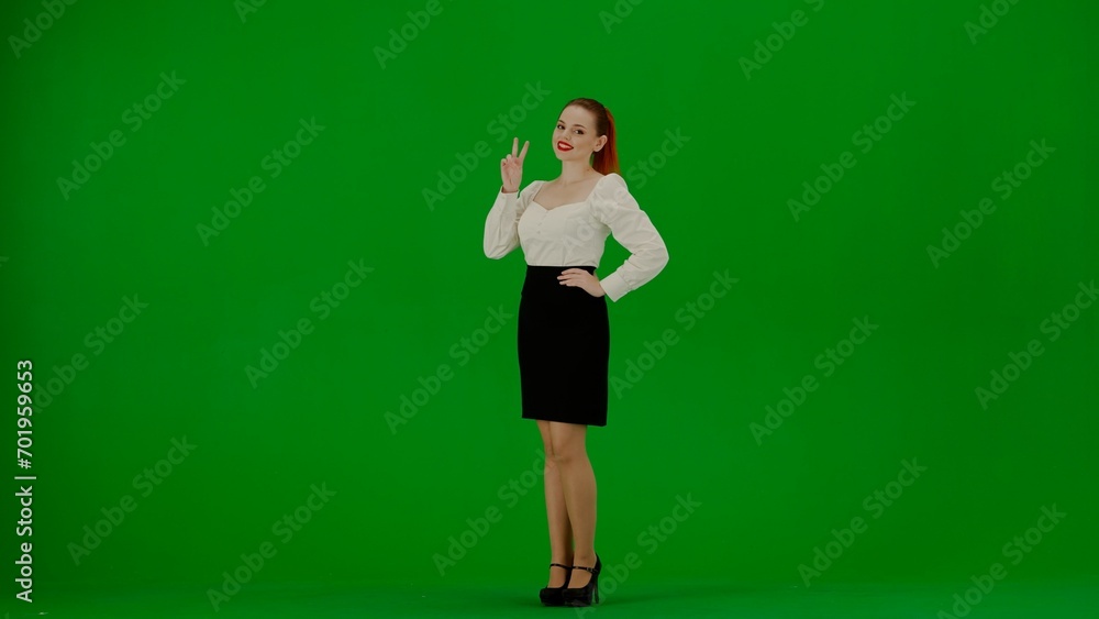 Portrait of attractive office girl on chroma key green screen. Woman in skirt and blouse standing smiling at camera showing victory sign. Portrait of attractive office girl on chroma key green screen. Woman in skirt and blouse standing smiling at camera showing victory sign.