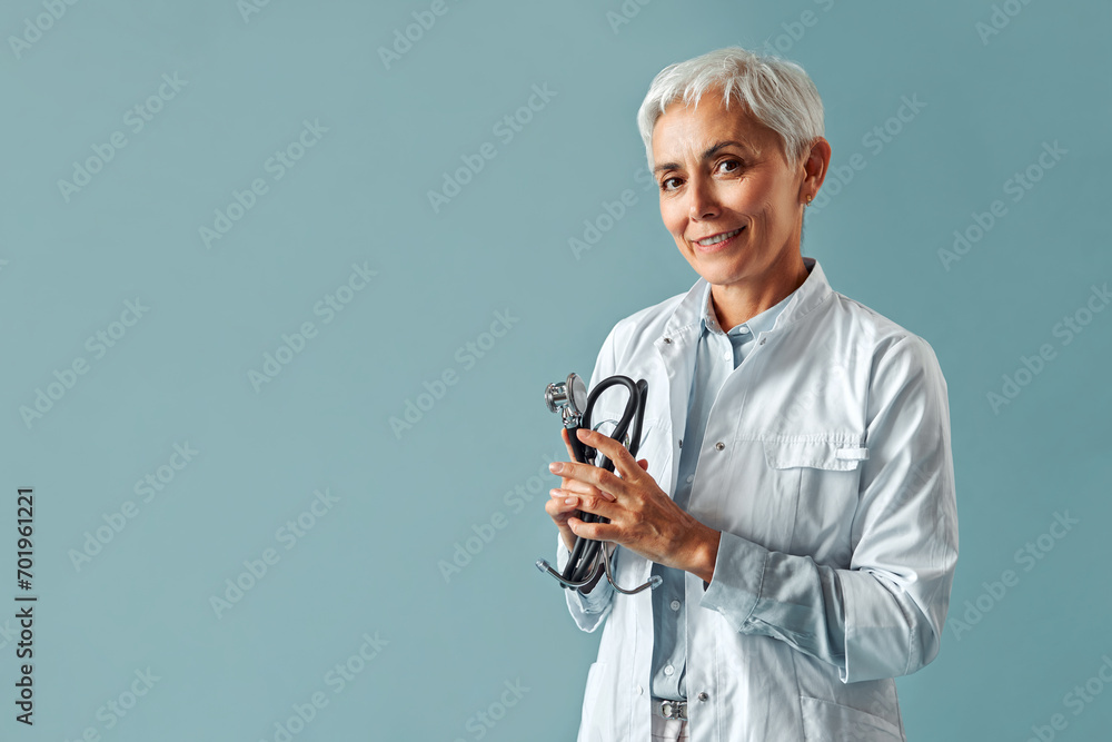 A female professional doctor in a white coat stands on a blue background and holds a stethoscope. Medical staff of the clinic. A female professional doctor in a white coat stands on a blue background and holds a stethoscope. Medical staff of the clinic.