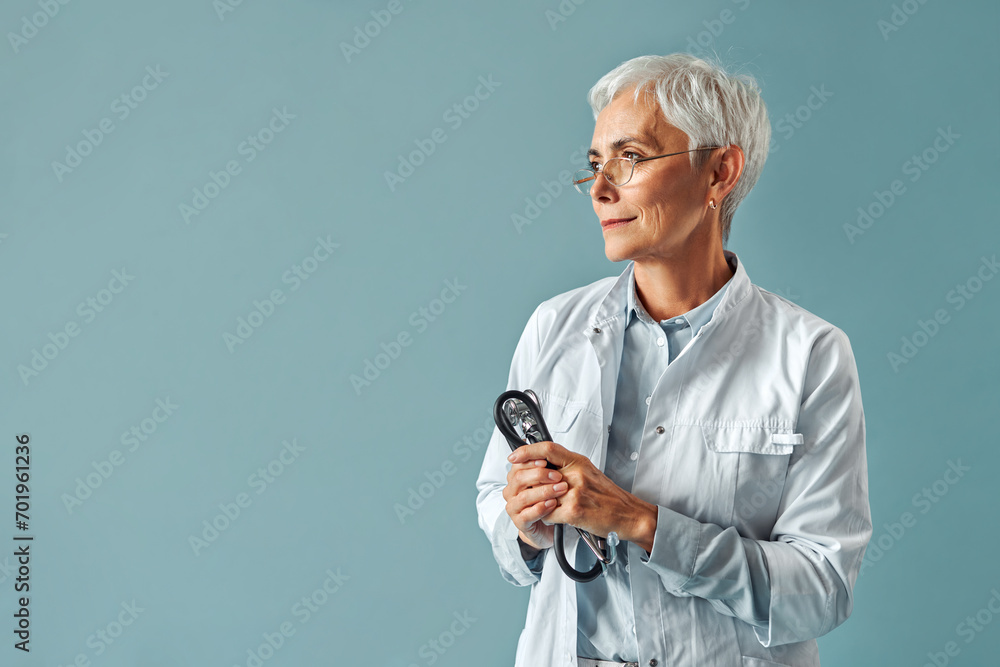 Gray-haired beautiful doctor woman in glasses looks to the side holding a stethoscope in her hands. Confidence and trust.General practitioner.