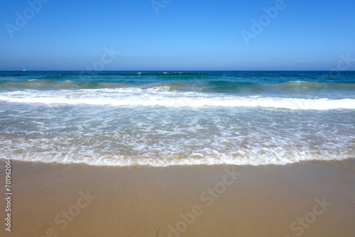 Gentle ocean breeze pushes rolling waves slowly toward wet sand of Pacific beach in San Diego, California