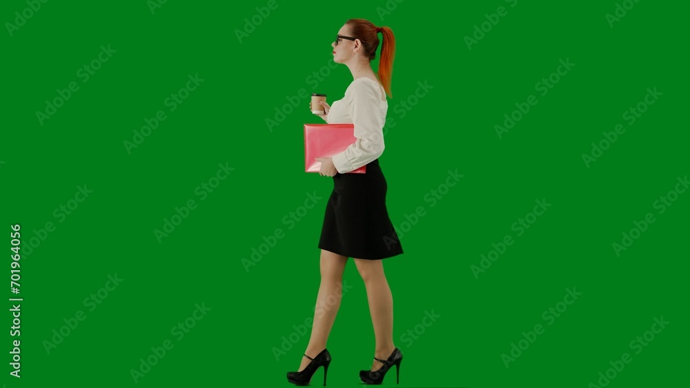 Portrait of attractive office girl on chroma key green screen. Woman in skirt and glasses walking holding red folder and coffee cup. Side view. Portrait of attractive office girl on chroma key green screen. Woman in skirt and glasses walking holding red folder and coffee cup. Side view.