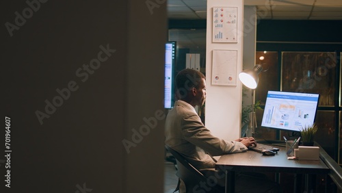 Revealing shot of employees checking company figures, postings and documents for accuracy during nighshift. Staff member working overnight, analyzing stored computerized financial information photo