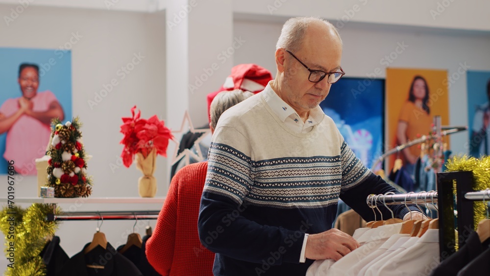 Elderly couple happy after finding perfect Christmas gift for son while shopping in Christmas decorated clothing store. Clients browsing through clothes during winter holiday season Elderly couple happy after finding perfect Christmas gift for son while shopping in Christmas decorated clothing store. Clients browsing through clothes during winter holiday season