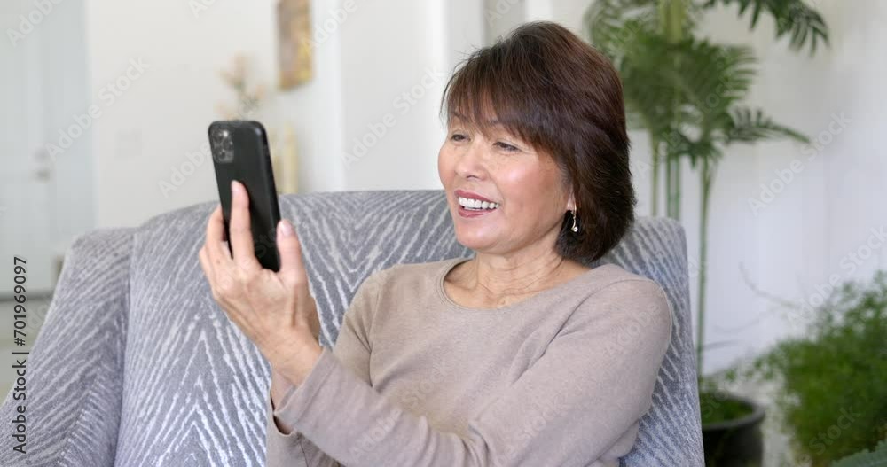 Cheerful attractive woman happy smiling talking FaceTime video chat using mobile cell phone laughing sitting in home living room. Cheerful attractive woman happy smiling talking FaceTime video chat using mobile cell phone laughing sitting in home living room.