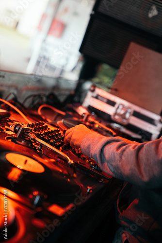 DJ ajustando el mixer junto a un disco de vinilo girando en un tocadiscos en un club con luz roja