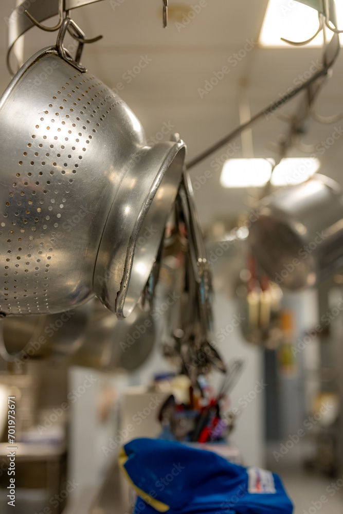 Stainless steel pots and pans and other cooking utensils hanging in a commercial industrial kitchen. Stainless steel pots and pans and other cooking utensils hanging in a commercial industrial kitchen.