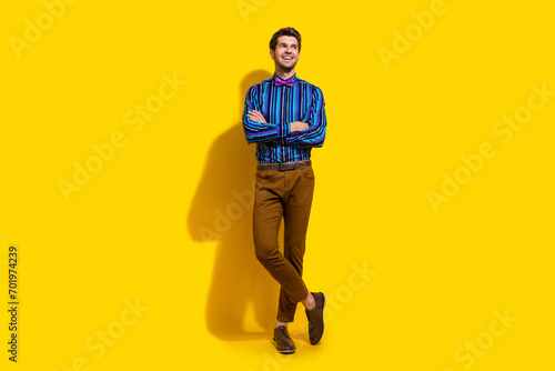Full size photo of cheerful guy dressed striped shirt trousers arms folded look at offer empty space isolated on yellow color background
