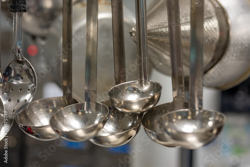 Stainless steel cooking utensils hanging in a commercial industrial kitchen. 