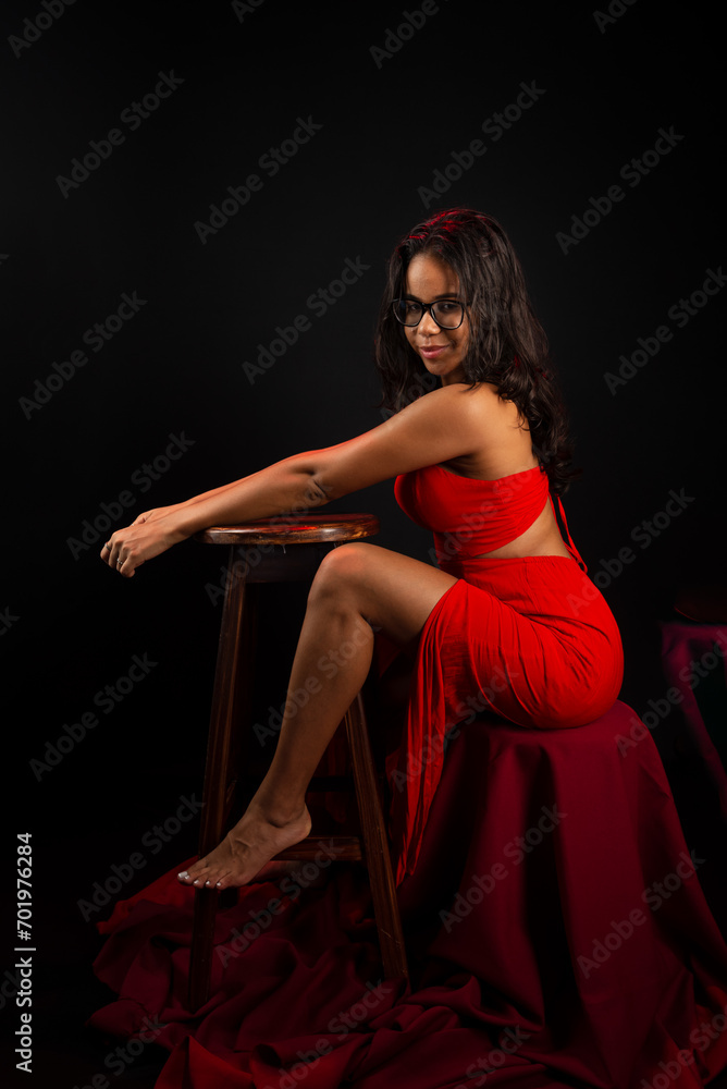 Portrait of beautiful young woman wearing glasses and in red dress sitting posing for photo.