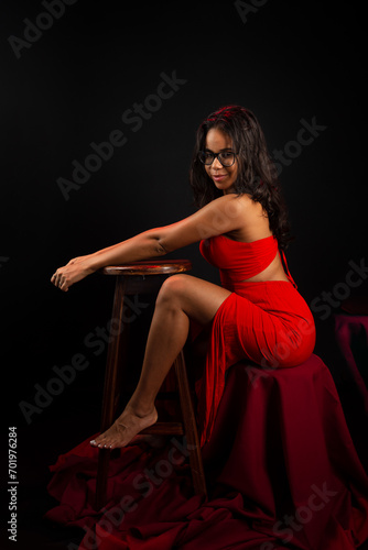 Portrait of beautiful young woman wearing glasses and in red dress sitting posing for photo.