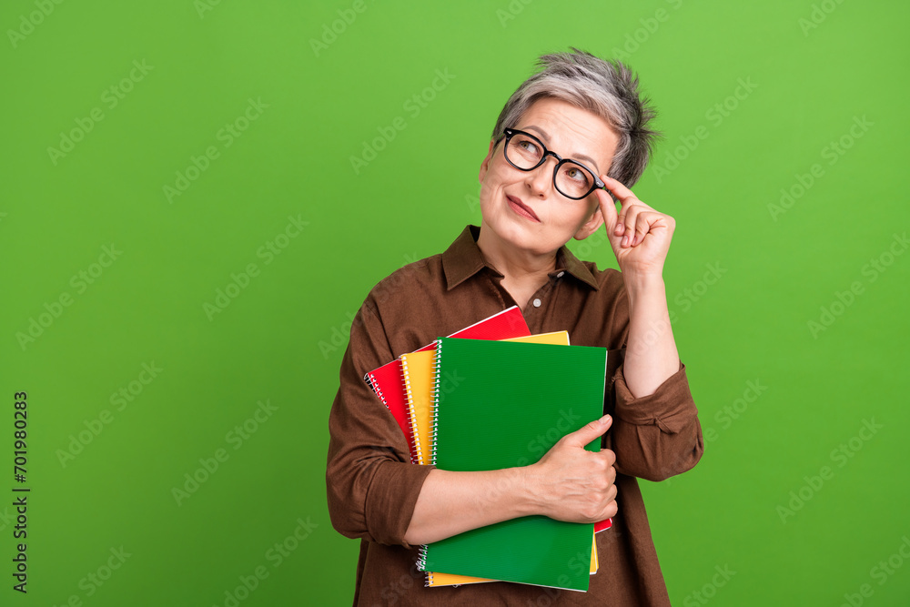 Portrait of minded person with white gray hairstyle touch glasses hold notebooks look empty space isolated on green color background Portrait of minded person with white gray hairstyle touch glasses hold notebooks look empty space isolated on green color background