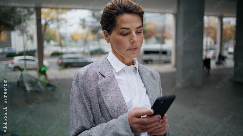 Serious businesswoman messaging smartphone on street. Focused woman typing cell
