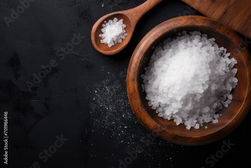 Top view of sea salt in wooden olive bowl on black background