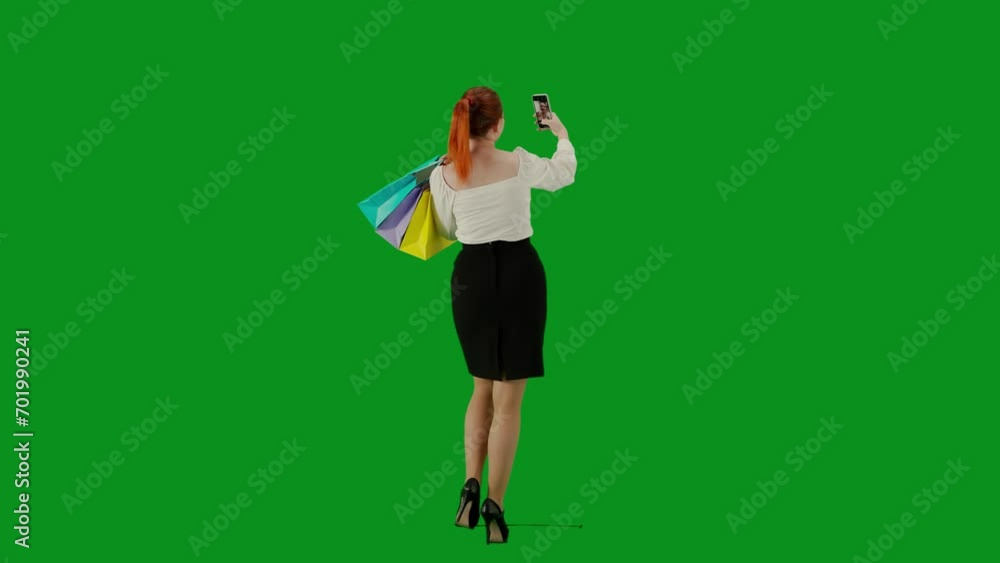 Portrait of attractive office girl on chroma key green screen. Woman in skirt walking holding gift bags taking selfie on smartphone. Back view. Portrait of attractive office girl on chroma key green screen. Woman in skirt walking holding gift bags taking selfie on smartphone. Back view.