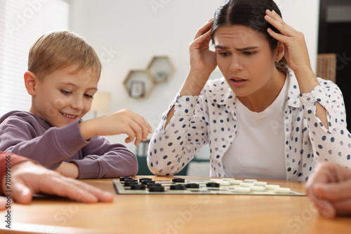 Family playing checkers at wooden table in room