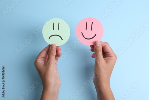 Choice concept. Woman holding papers with sad and happy emoticons on light blue background, top view