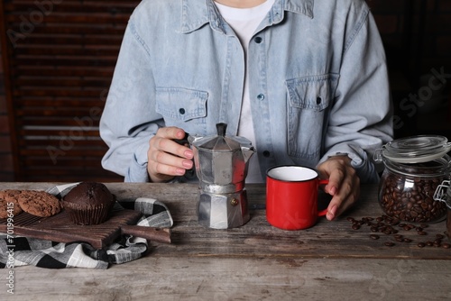 Brewing coffee. Woman with moka pot, cup, cookies and muffin at wooden table, closeup