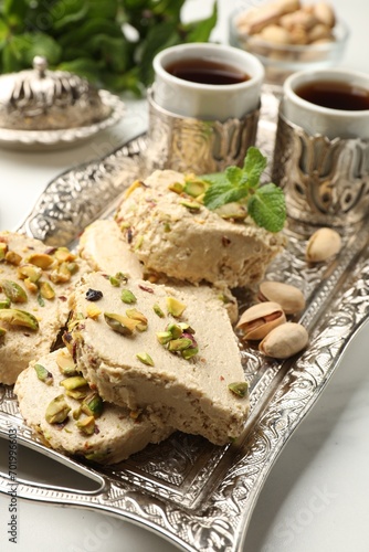 Tasty halva with pistachios and mint served on white table, closeup