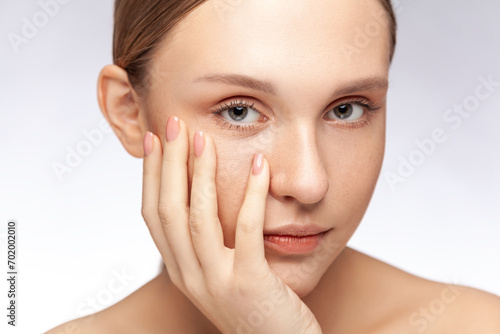 Closeup portrait of serious beautiful woman with natural makeup keeps hand under chin looking at camera with calm expression. Indoor studio shot isolated over gray background.