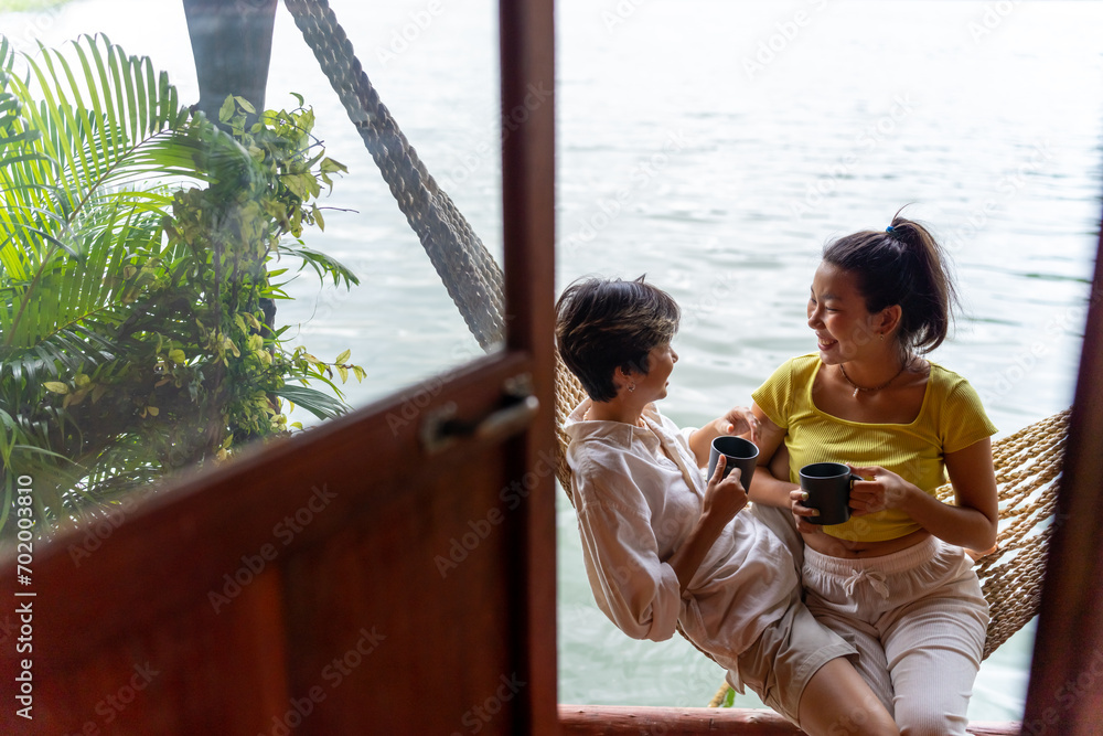 Obraz premium Happy Asian LGBTQ couple relaxing on hammock together at lake house balcony. People enjoy and fun outdoor lifestyle travel nature on summer holiday vacation. LGBT person and pride day concept.