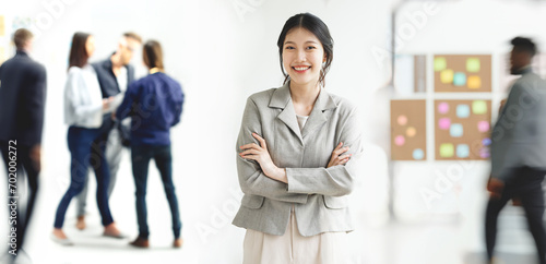Portrait of young white woman with arms crossed stanging in a busy modern workplace photo