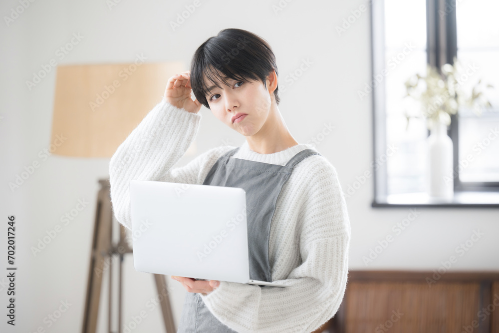 部屋でパソコンを使い、売上などを困る・悩む表情のショップの販売員や接客業のような女性 部屋でパソコンを使い、売上などを困る・悩む表情のショップの販売員や接客業のような女性